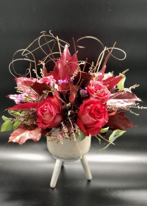 Σύνθεση λουλουδιών σε κόκκινες αποχρωσεις σε πέτρινο ποτ με ξύλινα πόδια 30€